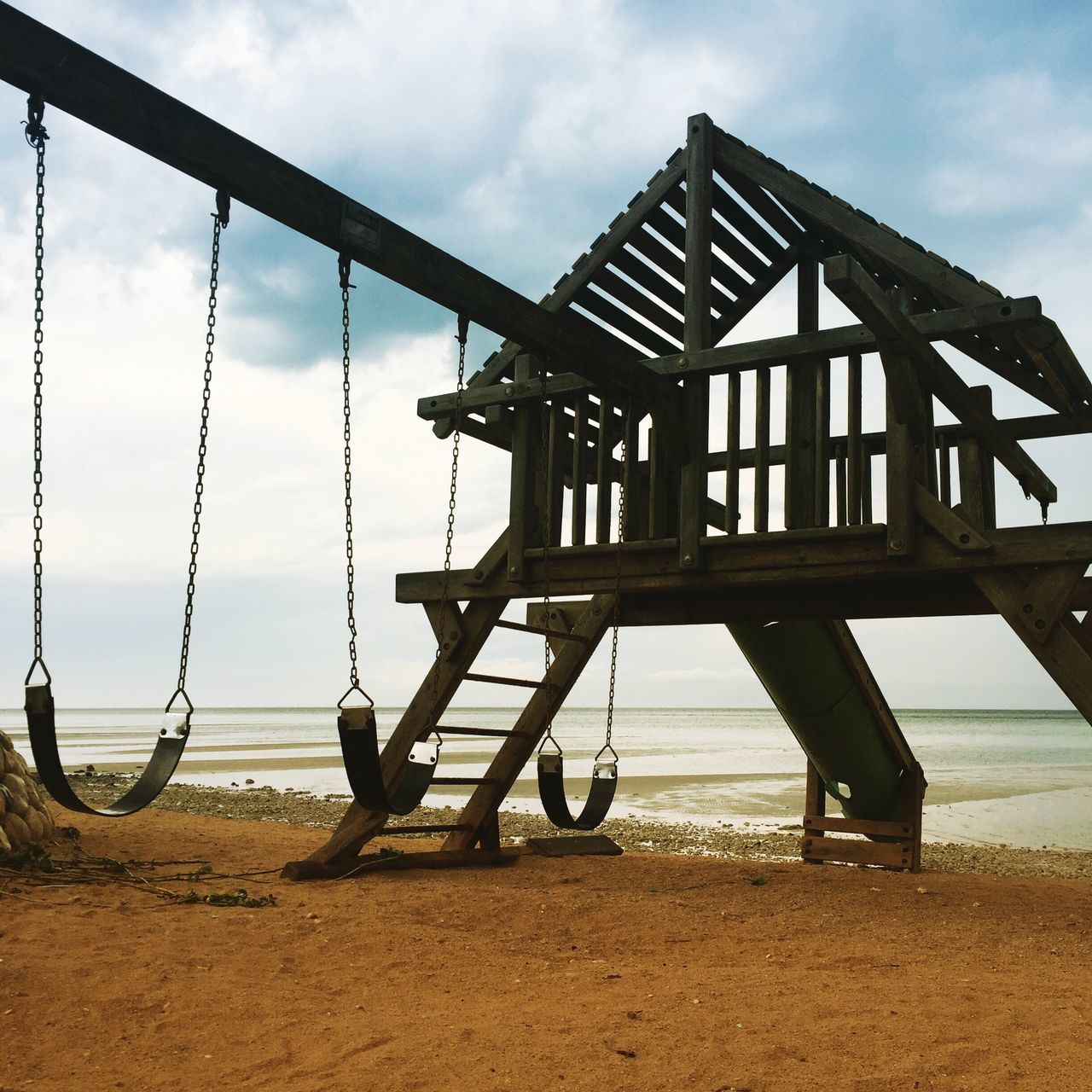 playground, sky, built structure, sand, outdoors, metal, day, childhood, outdoor play equipment, beach, no people, swing, sea, architecture, cloud - sky, jungle gym, city, nature