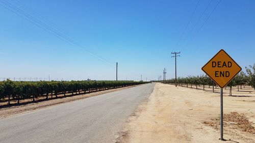 Dead end sign on road against clear blue sky