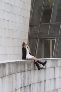 Side view of woman sitting on staircase against wall