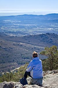 Rear view of woman sitting on rock against sky