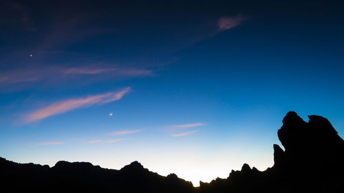 Low angle view of silhouette mountain against blue sky