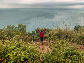 Rear view of person standing by sea against sky