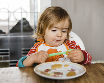 Cute girl eating food on table at home