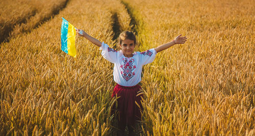 Portrait of smiling girl holding ukrainian flag standing on field