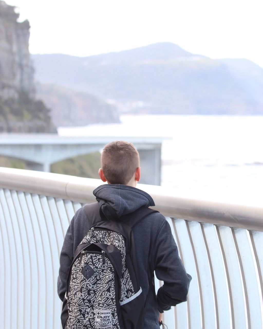 REAR VIEW OF MAN STANDING ON RAILING AGAINST CITYSCAPE