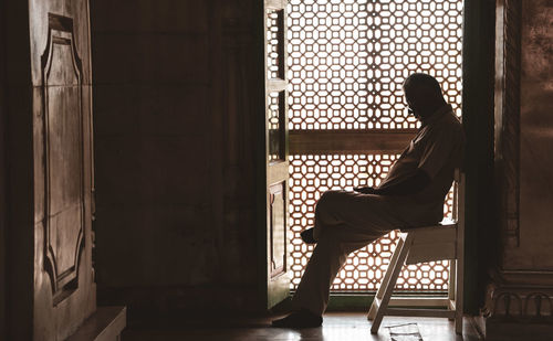 Side view of man sitting on chair against building