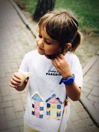 Cute girl holding ice cream standing on footpath