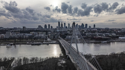 Bridge over river in city against cloudy sky