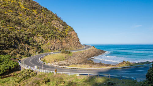 Scenic view of road by sea against clear blue sky