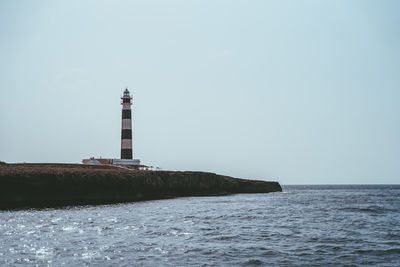 Lighthouse by sea against clear sky