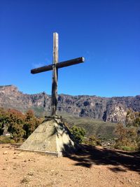 Cross on road against clear blue sky