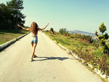 Rear view of woman walking on road against sky