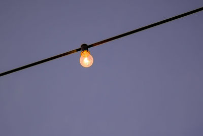 Low angle view of illuminated light bulb against clear sky