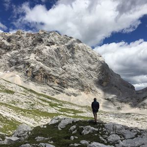 Rear view of man standing on rocks against cloudy sky