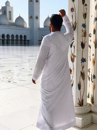 Rear view of man standing in mosque, in traditional clothes 