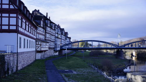 Bridge over river by buildings against sky