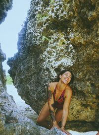 Smiling woman in swimsuit kneeling on rock at beach