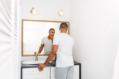 Rear view of young man looking in mirror at home