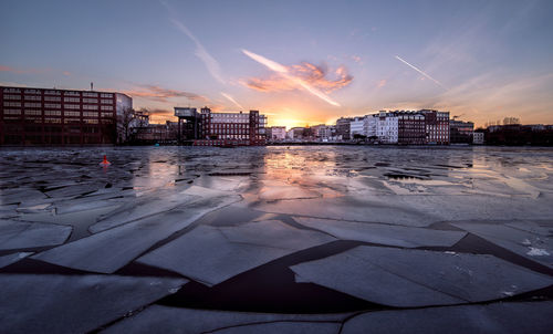 Frozen lake river against buildings at sunset