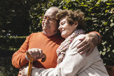 Senior couple sitting on bench in a park, with arms around