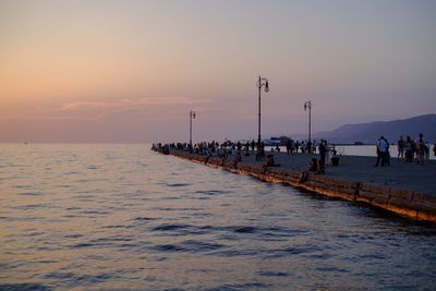People on pier at sea against sky during sunset 