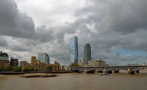 Bridge over river by buildings against cloudy sky