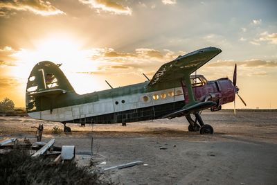 Abandoned airplane at beach against sky during sunset