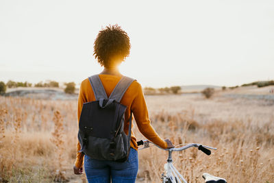 Young woman with bicycle standing in field at sunset