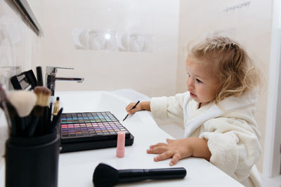 Toddler girl doing herself makeup with mama's cosmetics pretending grownup. applying eyeshadows