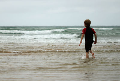 Rear view of boy walking in sea