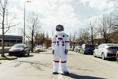 Young male astronaut in space suit standing on road at street during sunny day