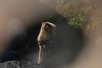 Beautiful young woman sitting in rock against plants