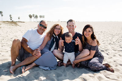 Family of five sitting on beach smiling for camera