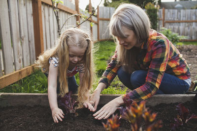 Girl with mother planting in raised bed at backyard
