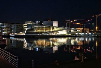 Illuminated buildings by river against sky at night