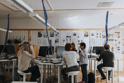 Teacher standing amidst students using computers at lab