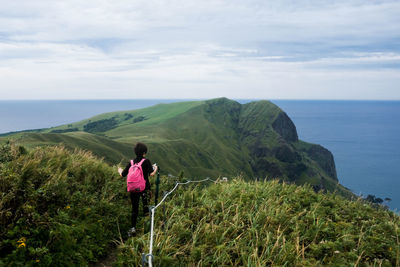 Rear view of woman hiking on mountain by sea against cloudy sky