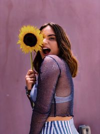 Portrait of woman holding sunflower while making face against wall