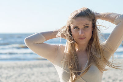 Portrait of woman with hand in hair standing at beach against sky