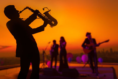 Silhouette people playing at music concert against sky during sunset