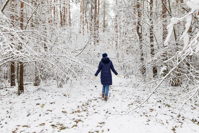 Rear view of woman walking on snow covered field in forest