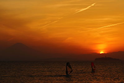 Silhouette people on sea against orange sky