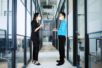 Full length of colleagues wearing mask standing in office