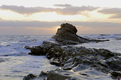 Rock formation on beach against sky during sunset