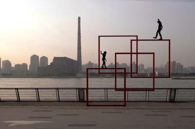 Silhouette sculpture by river against sky during sunset