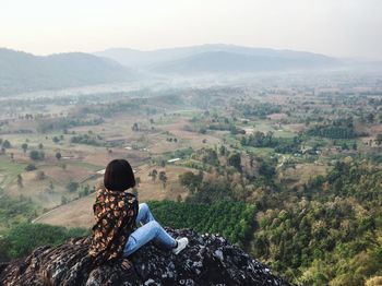 Woman sitting on mountain against sky