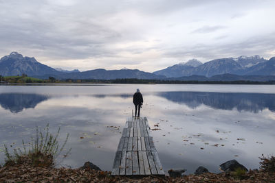 Rear view of woman standing on pier by lake against sky