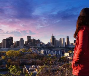 Rear view of woman standing by cityscape against sky during sunset