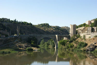 Arch bridge over river amidst buildings against clear sky