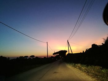 Road by silhouette trees against clear sky during sunset